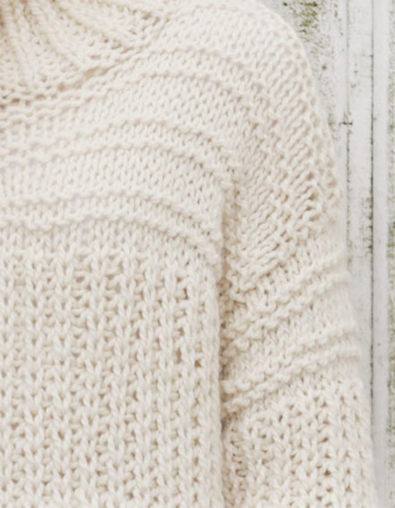 May include: A close-up of a cream-colored knitted sweater with a textured stitch pattern.