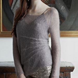 May include: A soft, light purple knitted sweater with a loose fit and a slightly scooped neckline. The sweater has a delicate, almost see-through texture.