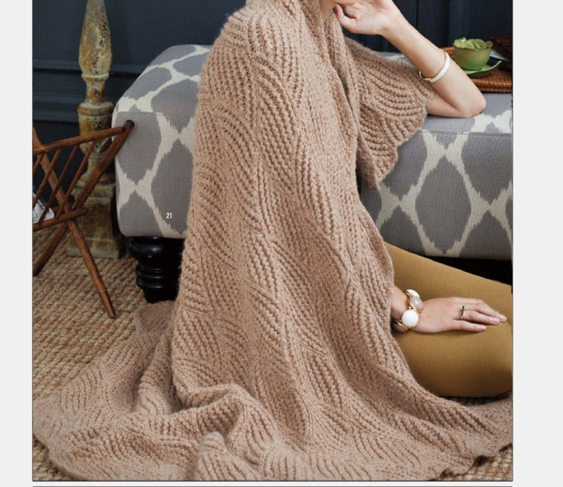 May include: A brown knitted throw blanket with a chevron pattern. The blanket is draped over a gray and white patterned ottoman.