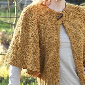 May include: A mustard yellow knitted cardigan with a wooden button closure. The cardigan has a relaxed fit and a slightly cropped length.