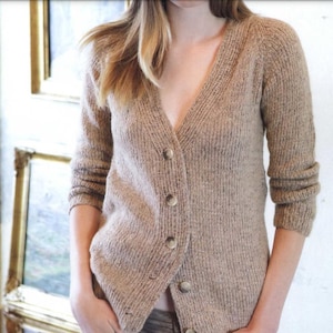 Può includere: Un cardigan beige con bottoni e scollo a V. Il maglione presenta una trama a maglia a coste ed è realizzato con un filato morbido dai toni neutri. I bottoni sono dello stesso colore. Le maniche sono a tre quarti.