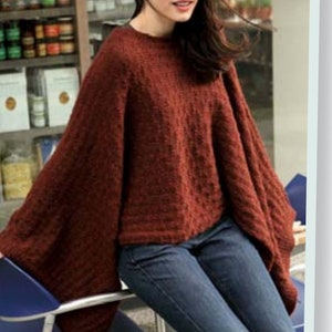 Può includere: Una donna indossa un maglione di maglia largo di colore ruggine con maniche lunghe e spalle leggermente scese. Indossa jeans blu.