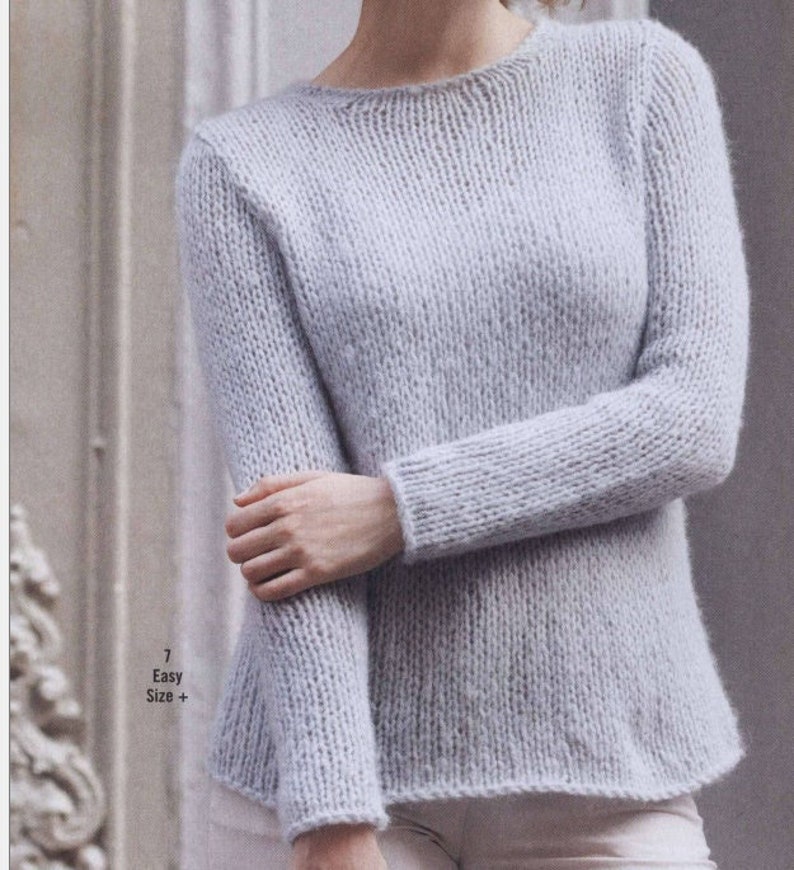 May include: A light blue knitted sweater with a round neckline and long sleeves. The sweater is made of a soft, fuzzy yarn and has a relaxed fit. The text "7 Easy Size+" is visible in the lower left corner of the image.