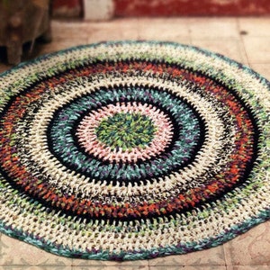 May include: A round, multi-coloured crocheted rug with a circular pattern. The rug is made of different coloured yarns, including white, black, green, orange, and pink.