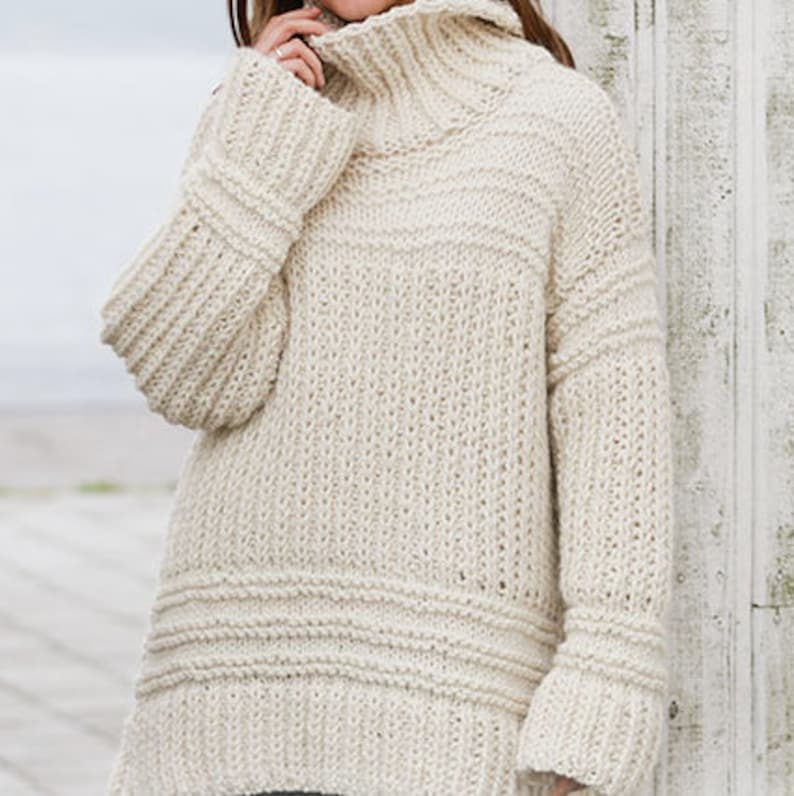 May include: A cream-colored knitted sweater with a high neck and long sleeves. The sweater has a relaxed fit and a ribbed texture.