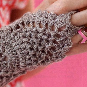 May include: A close-up of a brown crocheted fingerless glove with a lacy design. The glove is worn on a person's hand, which is also wearing several colorful chevron rings.
