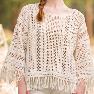 May include: A white crochet top with a loose fit and fringe trim. The top has a delicate openwork pattern and a round neckline.