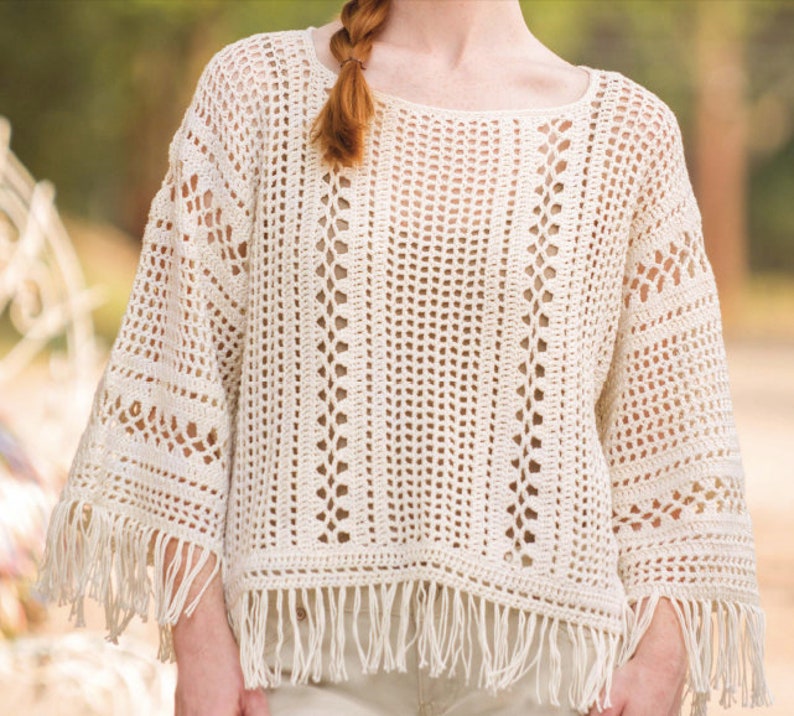 May include: A white crochet top with a loose fit and fringe trim. The top has a delicate openwork pattern and a round neckline.