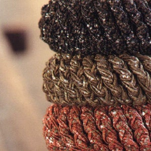 May include: Three stacked hair scrunchies in different colors and textures. The top scrunchie is black with a sparkly finish, the middle scrunchie is brown with a braided texture, and the bottom scrunchie is red with a braided texture.