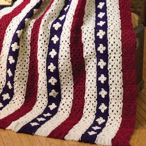 May include: A crocheted blanket with red, white, and blue stripes and a pattern of blue flowers. The blanket has a fringe border.