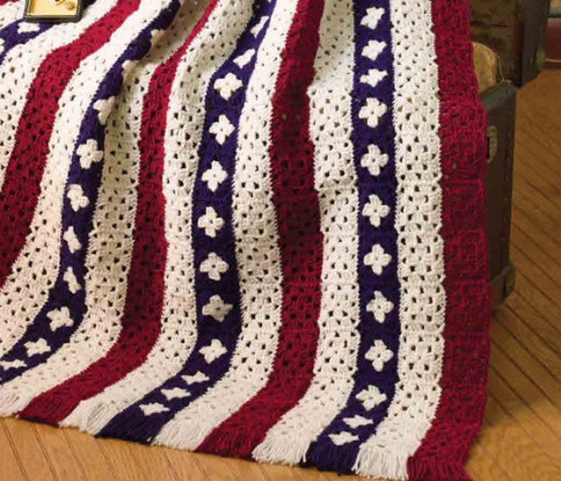 May include: A crocheted blanket with red, white, and blue stripes and a pattern of blue flowers. The blanket has a fringe border.