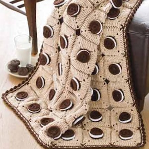 May include: A crocheted throw blanket with a brown and white cookie design. The blanket is made with a beige yarn and has a brown border.