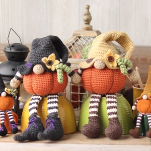 May include: Three crocheted pumpkin gnomes, one in black and orange, one in brown and orange, and one in green and orange, sitting on bowls. The gnomes are wearing hats and have yarn hair.