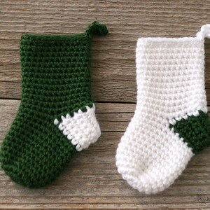 Two Mini Crocheted Stockings in green with a white heel and white with a green heel lying on a wooden background.