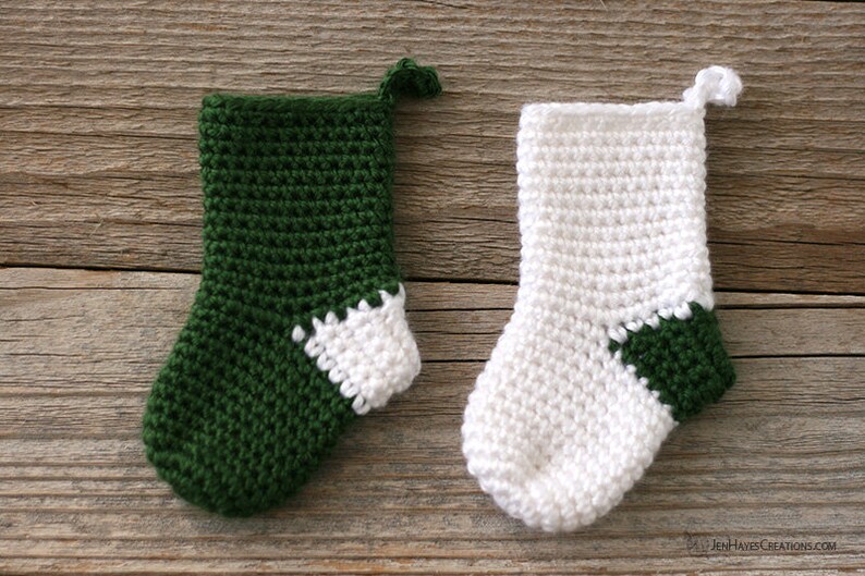 Two Mini Crocheted Stockings in green with a white heel and white with a green heel lying on a wooden background.