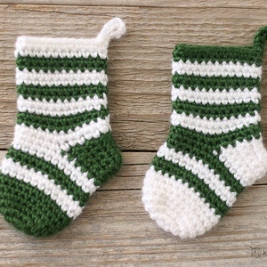 Two Mini Crochet Stockings in green and white stripes, one predominantly green and the other white, lying on a wooden background.