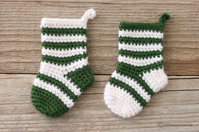 Two Mini Crochet Stockings in green and white stripes, one predominantly green and the other white, lying on a wooden background.