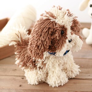 May include: A brown and white yarn dog toy with a blue collar. The dog toy is sitting on a wooden surface.