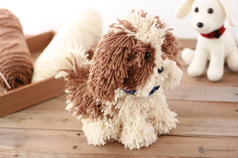 May include: A brown and white yarn dog toy with a blue collar. The dog toy is sitting on a wooden surface.