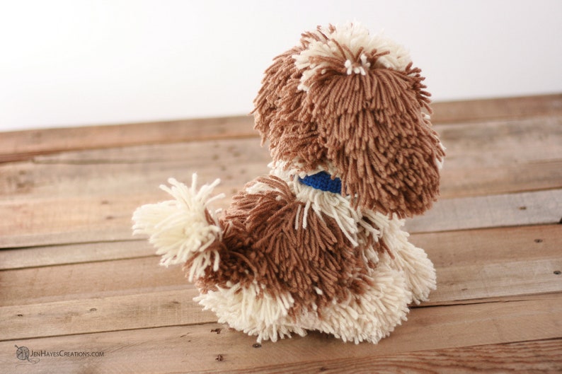 May include: A brown and white yarn dog toy with a blue collar. The toy is sitting on a wooden surface.