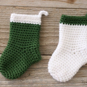 Two Mini Crocheted Stockings in green with a white top band and white with a green top band on a wooden background.