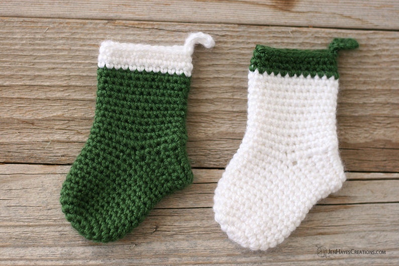 Two Mini Crocheted Stockings in green with a white top band and white with a green top band on a wooden background.