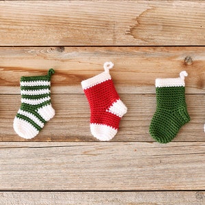 Five Mini Crochet Stockings in variations of red, green, and white solid, blocked, and striped designs lying on a wooden background.