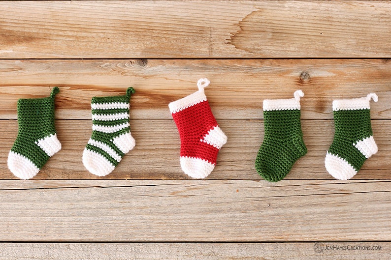 Five Mini Crochet Stockings in variations of red, green, and white solid, blocked, and striped designs lying on a wooden background.