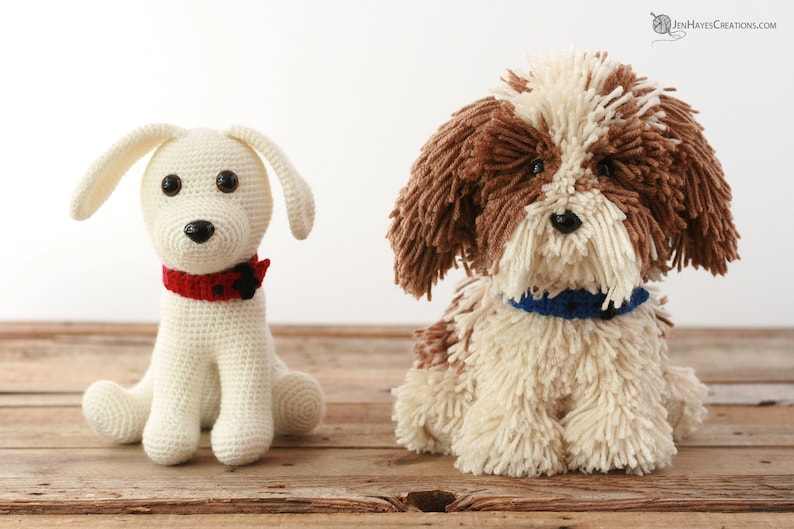 May include: Two crocheted stuffed dogs, one white with a red collar and the other brown and white with a blue collar. Both dogs are sitting on a wooden surface.