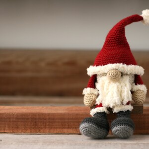 Crochet Santa Gnome sitting on a wood strip.