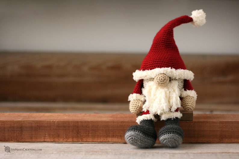 Crochet Santa Gnome sitting on a wood strip.