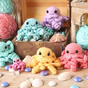 May include: A collection of crocheted octopus plushies in various colors, including pink, purple, yellow, and blue. The plushies are arranged on a wooden surface with seashells and glass beads.