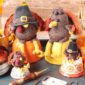 May include: Three crocheted turkeys wearing pilgrim hats, sitting on various surfaces. The turkeys are brown with red beaks and black eyes. The hats are black with a brown band. The surfaces are a yellow bowl, an orange bowl, and a white bowl with a floral design.