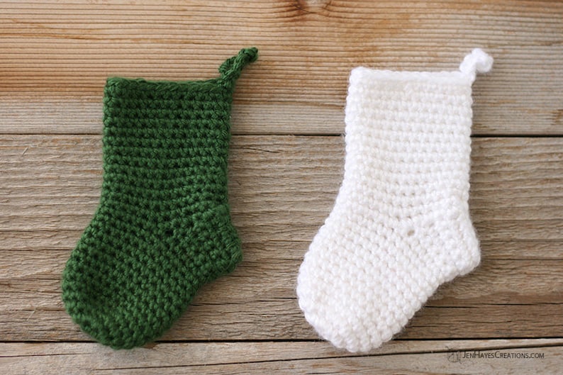 A solid dark green and a solid white Mini Crocheted Stocking laying on a wooden background.