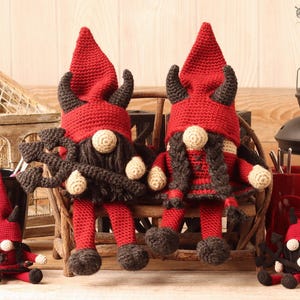 May include: Crocheted gnome figures with red hats and horns, black beards, and red and black outfits. The gnomes have white noses and are sitting on a wooden bench. The image includes yarn, crochet hooks, and decorative lanterns.