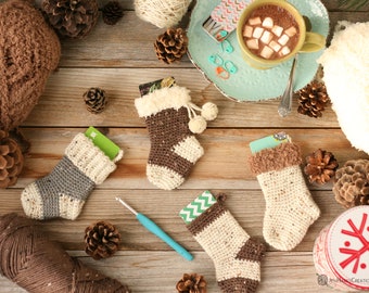 May include: Four crocheted Christmas stockings in brown and white with gift cards inside. The stockings are on a wooden surface with pine cones and yarn.