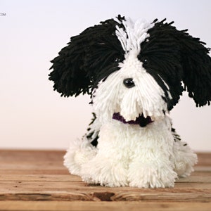 May include: A black and white yarn dog toy with a purple collar. The dog is sitting on a wooden surface.