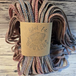 May include: A bundle of brown, pink, and blue wool yarn with a brown label that reads "Black Lily Woolens".
