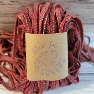 May include: A spool of red and cream wool yarn with a brown paper label that says "Black Lab Woolens".