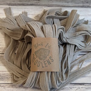May include: A pile of light gray wool yarn, with a brown label that reads "Black Lab Woolens".