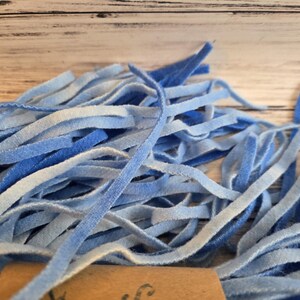 May include: A collection of thin, flexible strips in various shades of blue, ranging from light sky blue to deep royal blue. The strips have a soft, velvety texture and are bundled together, with a small portion of a brown paper tag visible at the base.