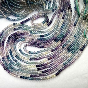 May include: A strand of round, faceted fluorite beads in shades of purple, blue, and green. The beads are strung on a thin thread and are approximately 4mm in diameter.