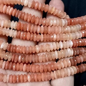 以下が含まれることがあります： 桃色のサンストーンビーズのネックレス。ビーズはファセットカットの涙型で、透明なゴム製のコードに糸に通されています。