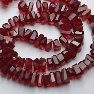 May include: A strand of deep red faceted gemstone beads. The beads are irregular in shape and have a glossy finish.