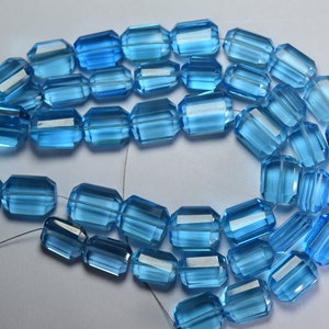 Pode incluir: Um fio de contas de vidro facetadas de cor azul claro. As contas são de forma retangular e têm um acabamento liso e polido.
