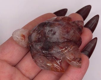 May include: A carved turtle figurine made of semi-translucent quartz with deep red and brown mineral inclusions throughout the stone. The turtle features a smooth, polished surface with visible natural crystalline patterns and internal fractures.
