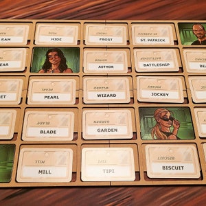 May include: A wooden board with 25 slots, each containing a card with a word printed on it. The words include "Ram", "Hide", "Frost", "St. Patrick", "Pearl", "Wizard", "Jockey", "Battleship", "Author", "Garden", "Blade", "Mill", "Tipi", and "Biscuit".