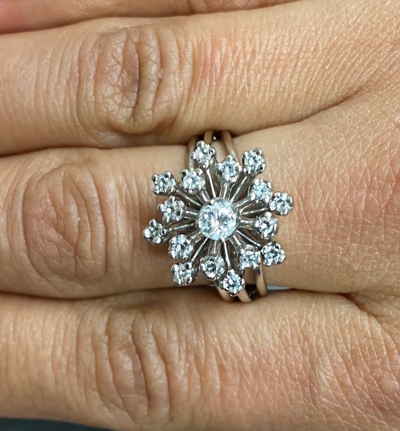 Może przedstawiać: Srebrny pierścionek z dużym, błyszczącym diamentem w środku, otoczonym mniejszymi diamentami w kształcie płatka śniegu.