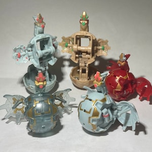 Puede incluir: Cuatro juguetes Bakugan de diferentes colores y configuraciones. Los juguetes están en su forma de bola cerrada, con algunos de los juguetes parcialmente abiertos para revelar sus mecanismos internos. Los juguetes están hechos de plástico y tienen un acabado metálico.