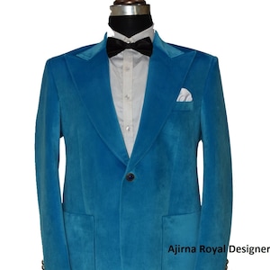 May include: A teal blue velvet blazer with a single button closure and a pocket on each side. The blazer has a shawl collar and a white pocket square. The text "Ajirna Royal Designer" is visible on the bottom right corner of the image.